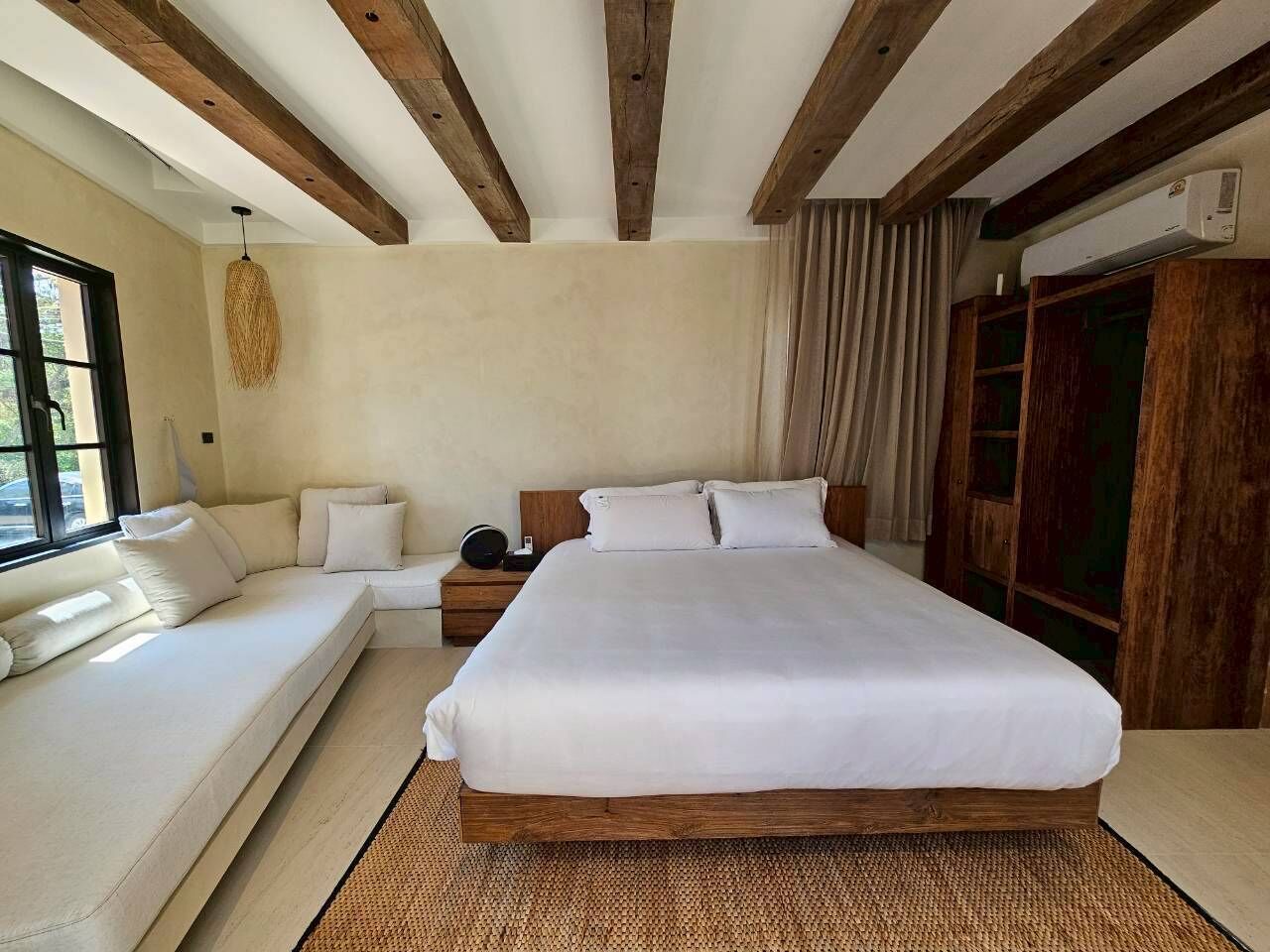 A bedroom with a large bed, a sofa, a bedside table, and a window.