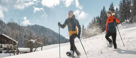 Two people skiing on a snowy slope with a cabin in the background.