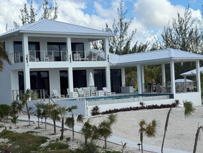 A two-story building with a pool, outdoor seating, and a beach view.