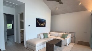 A spacious living room with a high ceiling, a ceiling fan, a large window, and a modern sofa set. - Spectacular Beachfront Ultra Luxury Villa Stella Maris-Introductory Sale! (Sandy Point)