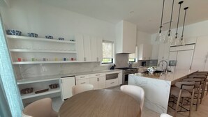 A modern kitchen with white cabinetry, a central island with bar stools, and a dining table with chairs. - Spectacular Beachfront Ultra Luxury Villa Stella Maris-Introductory Sale! (Sandy Point)