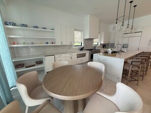 Una cocina moderna con armarios blancos, una isla central con taburetes y una mesa de comedor con sillas.