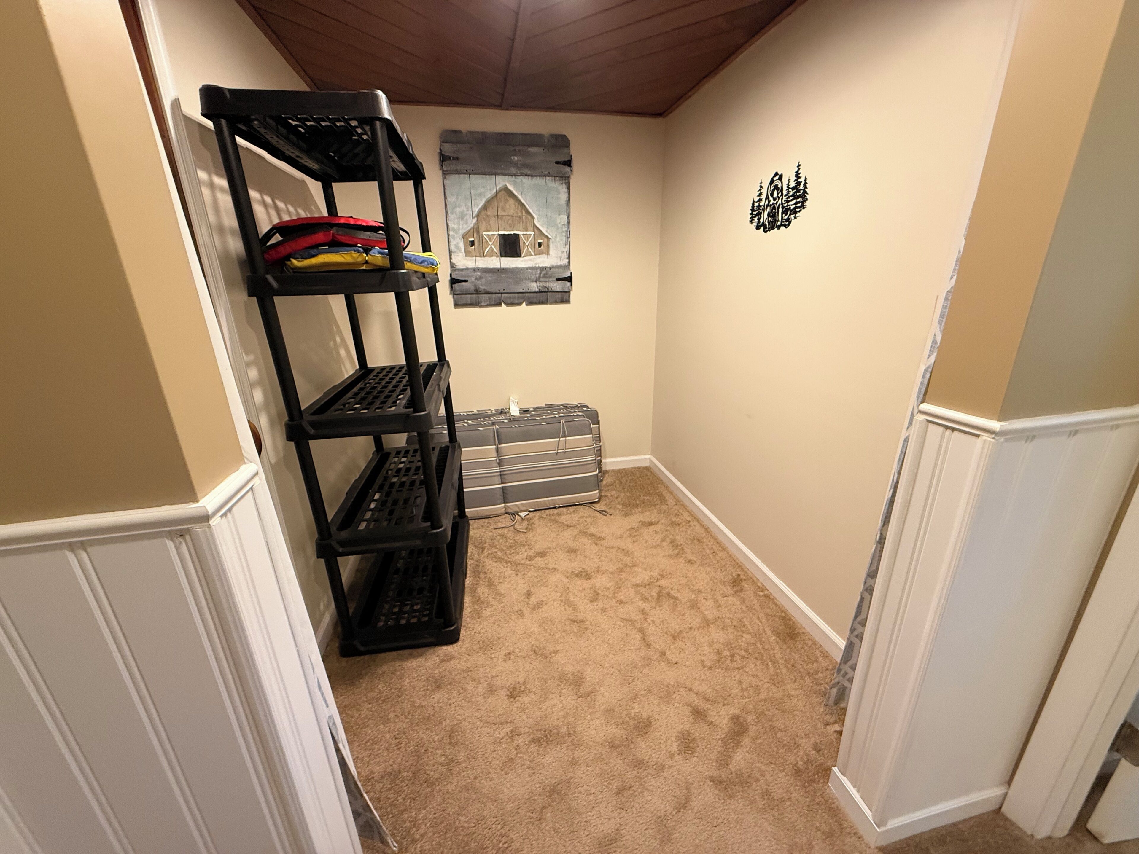 A room with a black metal shelf unit against the wall, a small rug, and a wall-mounted artwork depicting a barn.