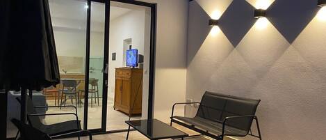 Un espacio al aire libre con una mesa, sillas, un banco y un televisor en un mueble.