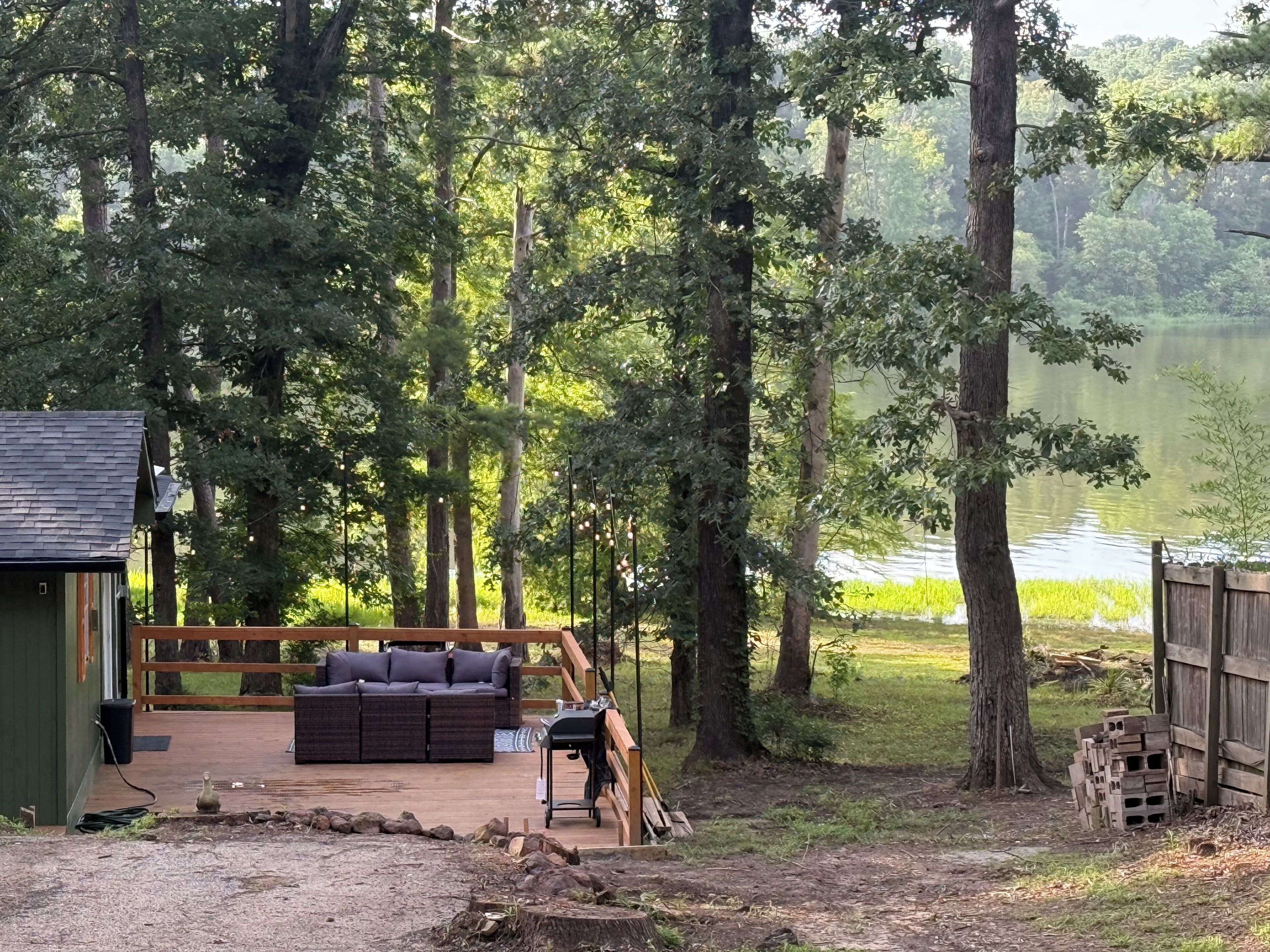 A deck with a sofa and grill, surrounded by trees and a lake.