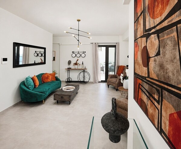 Una sala de estar moderna con un sofá verde, una mesa de centro y un espejo decorativo. Hay un cuadro abstracto y original en la pared y una lámpara de techo.
