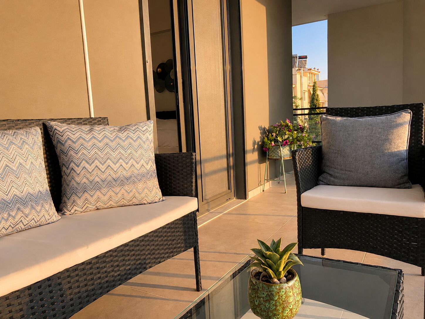 A balcony with wicker furniture, a glass table, and a potted plant.
