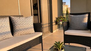 A balcony with wicker furniture, a glass table, and a potted plant.
