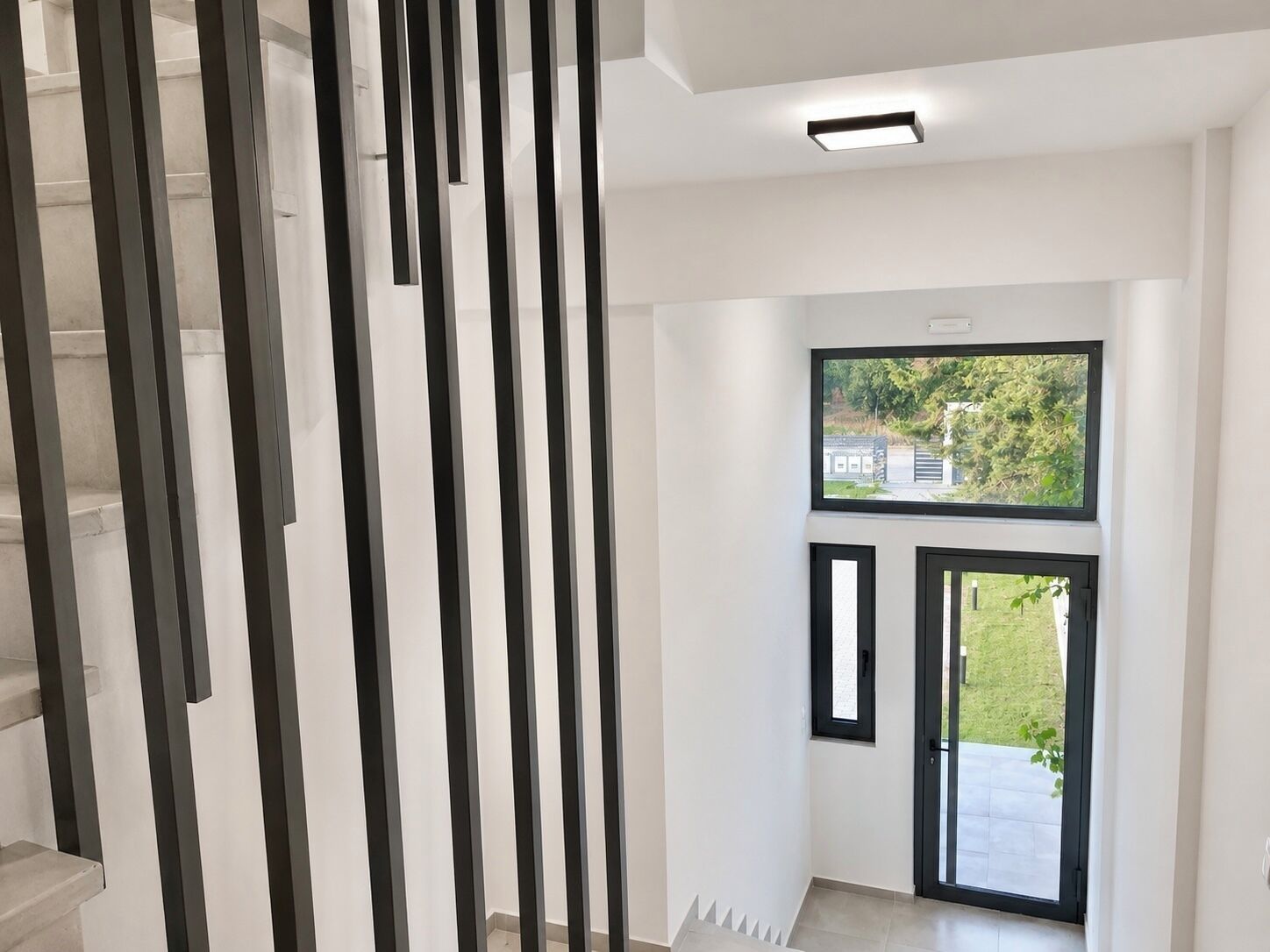Un intérieur moderne avec un escalier, un téléviseur à écran plat fixé au mur et une porte donnant sur un espace extérieur.