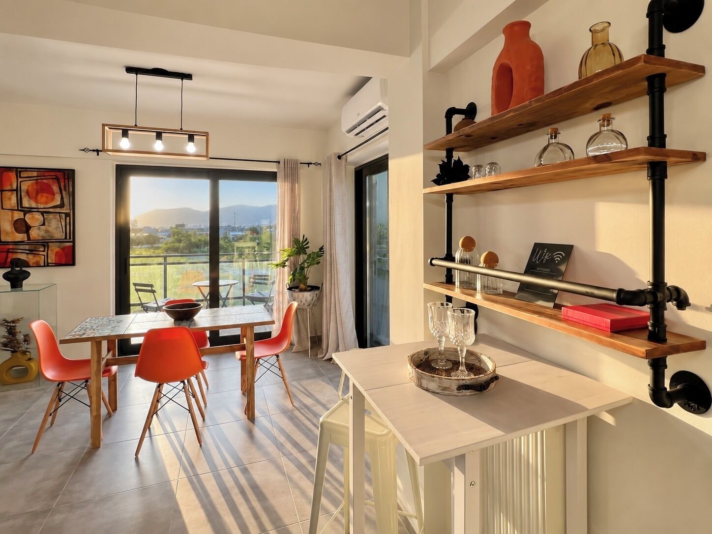 A modern dining area with a table and chairs, a hanging light fixture, and a view through a large window.