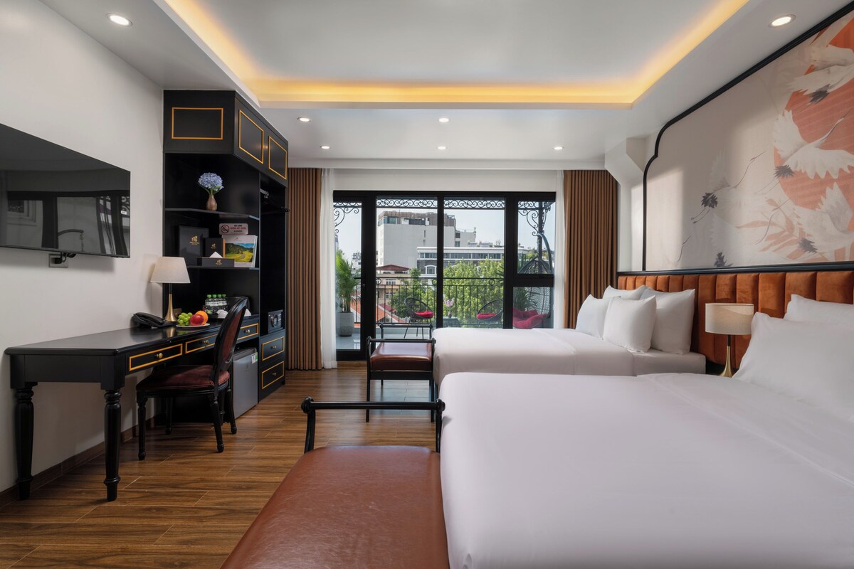 A hotel room with a desk, a bed, a chair, a bookshelf, and a large window with a view of buildings.