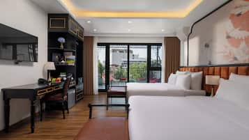 Habitación de hotel con escritorio, cama, silla, estantería y una ventana grande con vistas a edificios.