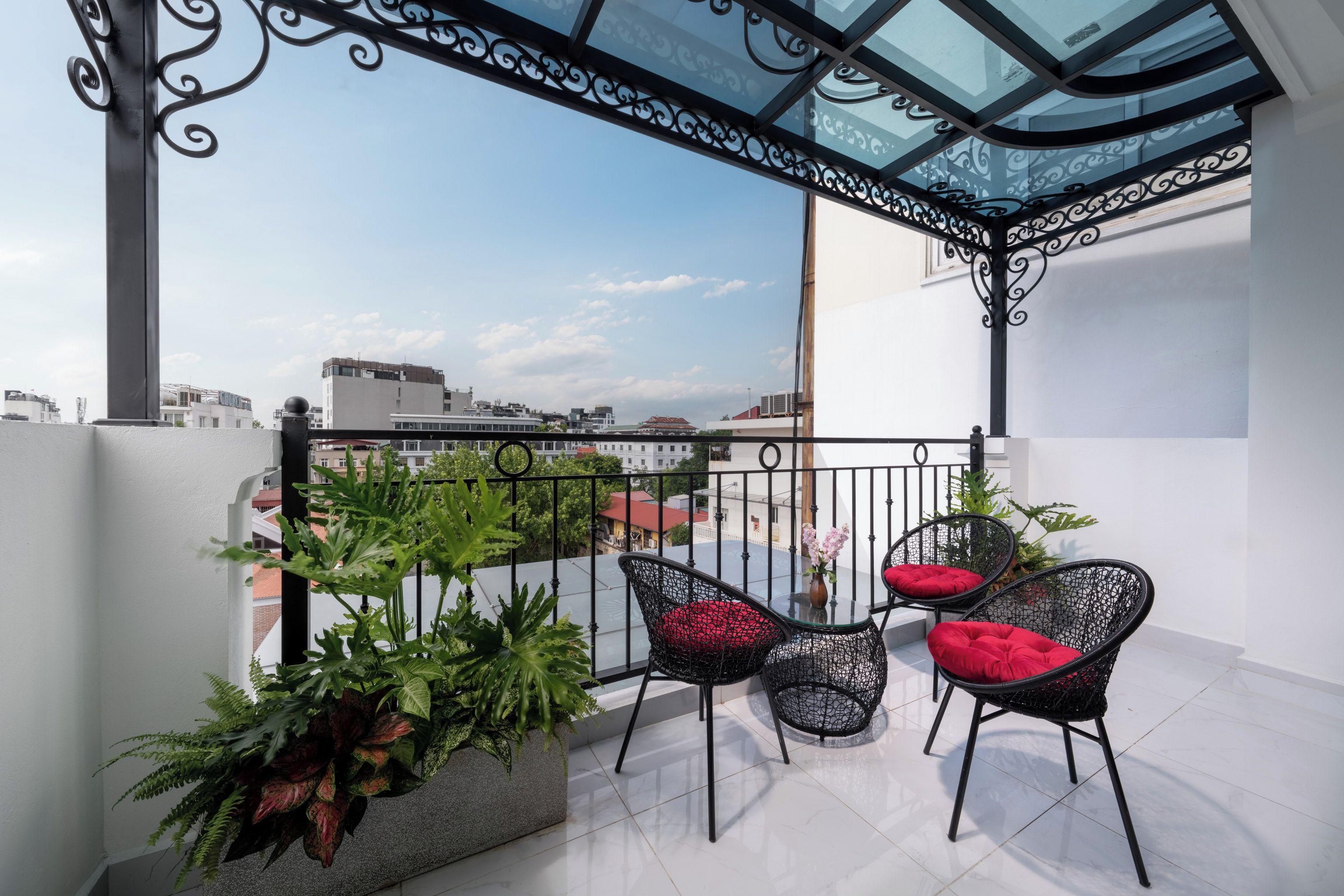 A balcony with two wicker chairs, a potted plant, and a glass table.