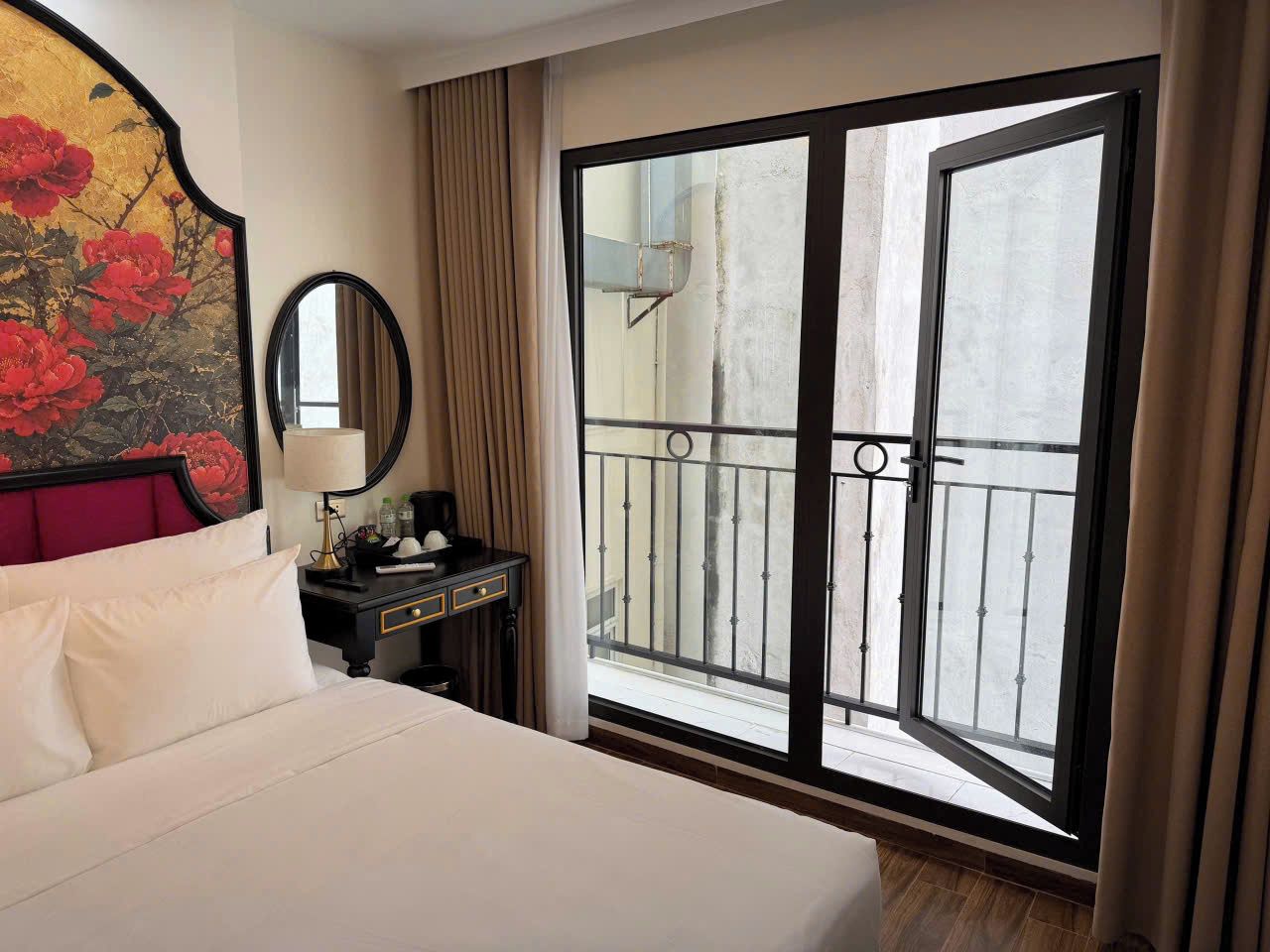 Una habitación de hotel con cama, mesita de noche, espejo, ventana con vistas al exterior y balcón.