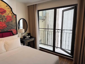 A hotel room with a bed, a nightstand, a mirror, a window with a view of the outside, and a balcony. - Alley Garden Hotel & Spa (Hanoi)
