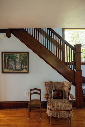 A wooden staircase with a railing, a wooden chair with a cushion, and a painting of a forest on the wall.