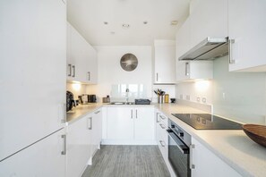 A modern kitchen with white cabinetry, a central island, a built-in oven, and a stainless steel range hood. - Top Floor Penthouse Near Stadium - Free Parking (London)