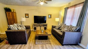 A living room with a ceiling fan, a flat-screen TV, two sofas, a coffee table, and a patterned rug.