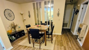 A dining area with a wooden table and chairs, a patterned rug, and a decorative wall piece.