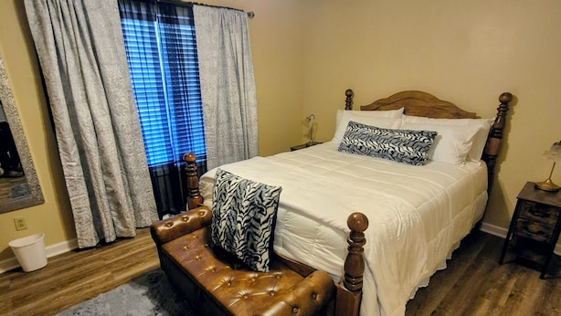 A bedroom with a bed, a bench, a ceiling fan, and a window with curtains.