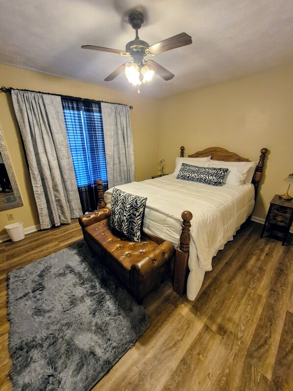 A bedroom with a bed, a bench, a ceiling fan, and a window with curtains.