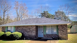 A single-story brick house with a gabled roof, green shutters, and a front porch.