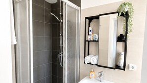 A modern bathroom with a glass-enclosed shower, a white sink, and a mirror with a shelf above it. - N&N: Apartment - in the heart of the Old Town (Wismar)