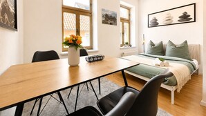 A modern living room with a dining table, chairs, a sofa with green cushions, and a bed with a green blanket. - N&N: Apartment - in the heart of the Old Town (Wismar)