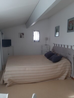 A bedroom with a bed, a television, a window, and a painting on the wall. - Vacation in Portiragne-Plage (Portiragnes)