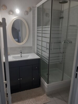A bathroom with a glass-enclosed shower, a round mirror, and a white sink. - Vacation in Portiragne-Plage (Portiragnes)