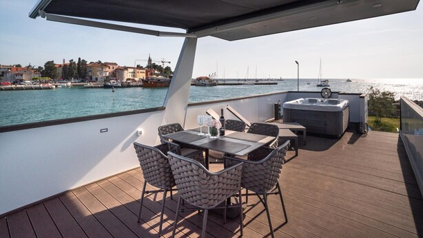A deck with a table and chairs, a hot tub, and a view of the water and buildings. - Modern Houseboat for 6 People (Novigrad)
