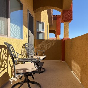 Ein Balkon mit zwei Stühlen, einem Tisch, einer Tür und einem Fenster mit Jalousien.