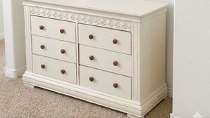 A white dresser with six drawers and a flat-screen TV mounted above it.