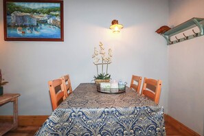 A dining area with a table set for four, a painting on the wall, and a wall-mounted light fixture. - Skylark (Liskeard)