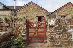 A stone building with a wooden pull gate, a stone wall with plants, and a sign reading 'SKY LAR'. - Skylark (Liskeard)