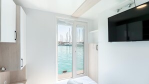 A modern hotel room with a bed, a TV, a door leading to a balcony with a view of boats, and a wooden ceiling. - Exclusive Houseboat Directly in the Marina (Novigrad)