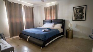 A modern bedroom with a bed, curtains, a ceiling fan, a bedside lamp, and a framed picture on the wall.