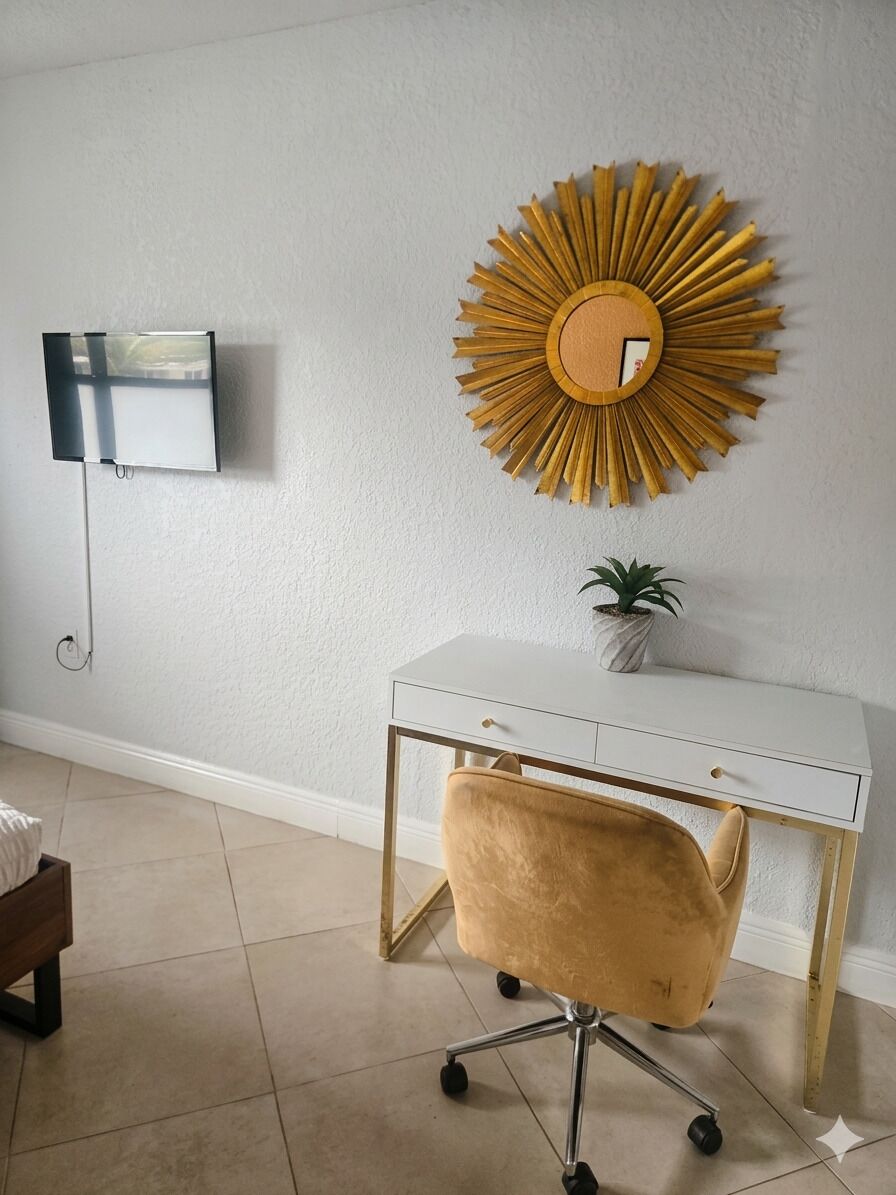 Une pièce avec un bureau blanc, une chaise dorée, un élément décoratif rond fixé au mur et une petite plante en pot.