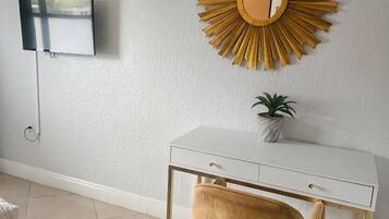 Une pièce avec un bureau blanc, une chaise dorée, un élément décoratif rond fixé au mur et une petite plante en pot.