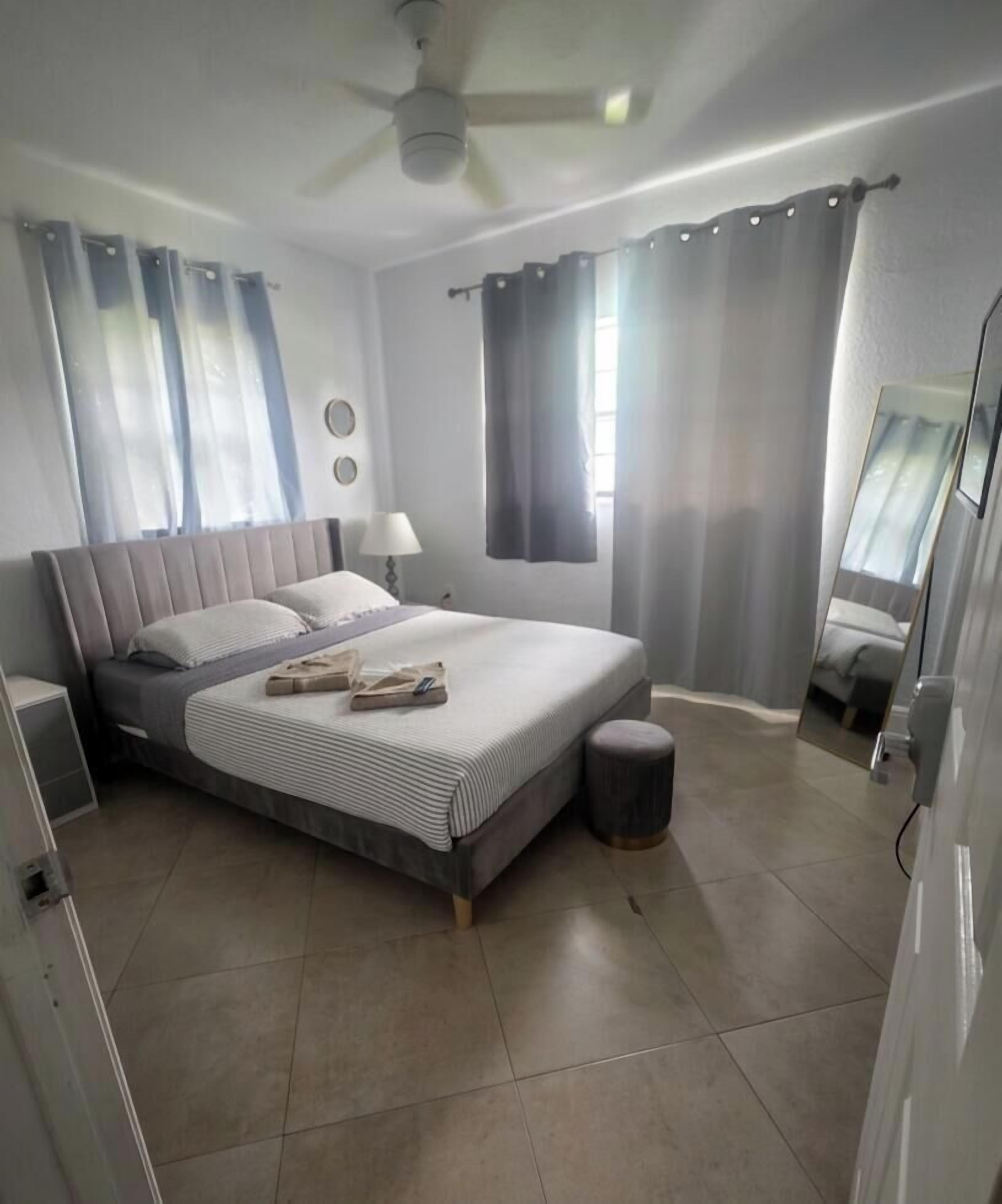 Une chambre à coucher avec un lit, des rideaux, un miroir et un ventilateur de plafond.