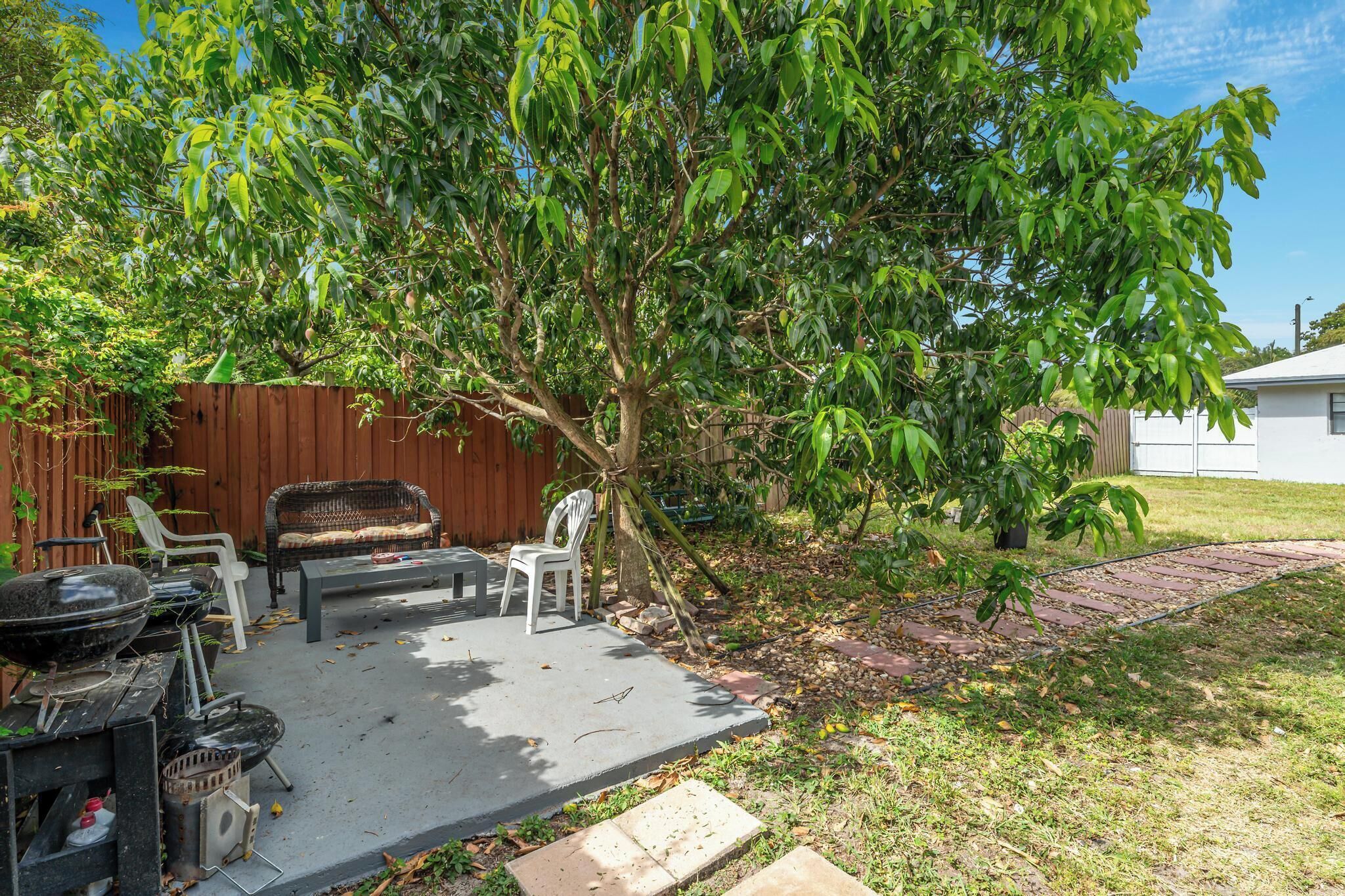 Une terrasse extérieure avec un barbecue, deux chaises, une table et un arbre.