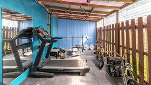 A covered outdoor gym area with exercise equipment, a bicycle, and a motorcycle.