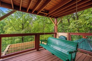 A wooden deck with a green bench and a view of a forest. - 🏔️ Mountain Views + Hot Tub | Loaded Game Room | Sleeps 10 (Pigeon Forge)