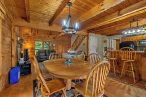 A wooden cabin interior with a dining table, chairs, a kitchen area, and a staircase. - 🏔️ Mountain Views + Hot Tub | Loaded Game Room | Sleeps 10 (Pigeon Forge)