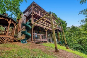 A wooden cabin with a spiral staircase and a deck. - 🏔️ Mountain Views + Hot Tub | Loaded Game Room | Sleeps 10 (Pigeon Forge)
