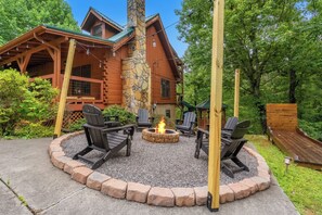 A wooden cabin with a stone chimney, surrounded by a fire pit and outdoor seating. - 🏔️ Mountain Views + Hot Tub | Loaded Game Room | Sleeps 10 (Pigeon Forge)