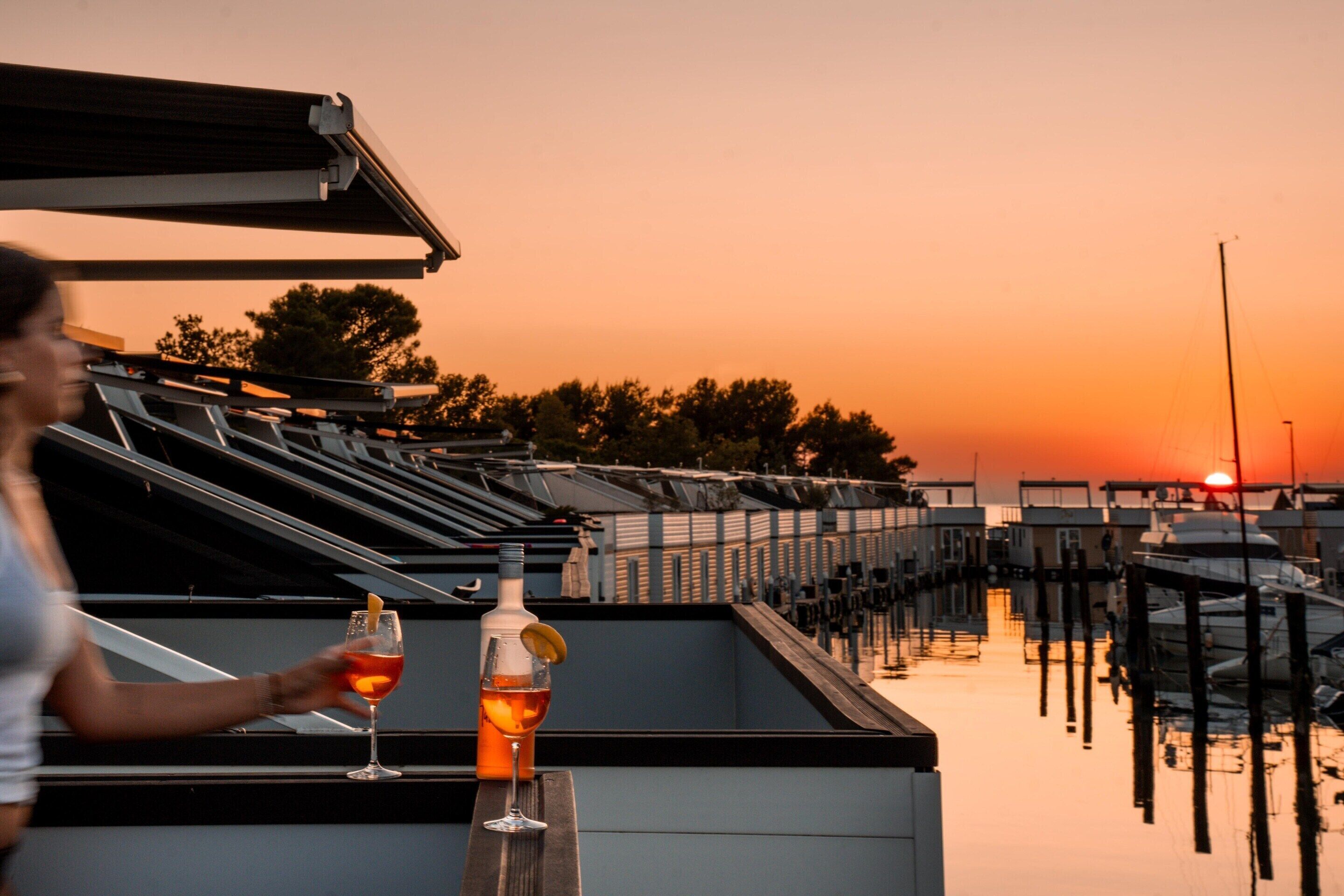 Une terrasse sur le toit offrant une vue sur le coucher du soleil, un verre de vin rouge et une bouteille de vin.