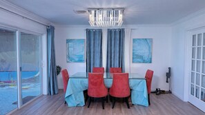 Uma sala de jantar com mesa de vidro e cadeiras vermelhas, um candelabro e duas pinturas abstratas na parede.