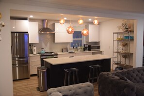 Uma cozinha moderna com eletrodomésticos de aço inoxidável, uma ilha central, banquetas e iluminação pendente.