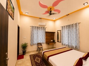 A hotel room with a bed, a chair, a desk, an air conditioning unit, and a ceiling fan.